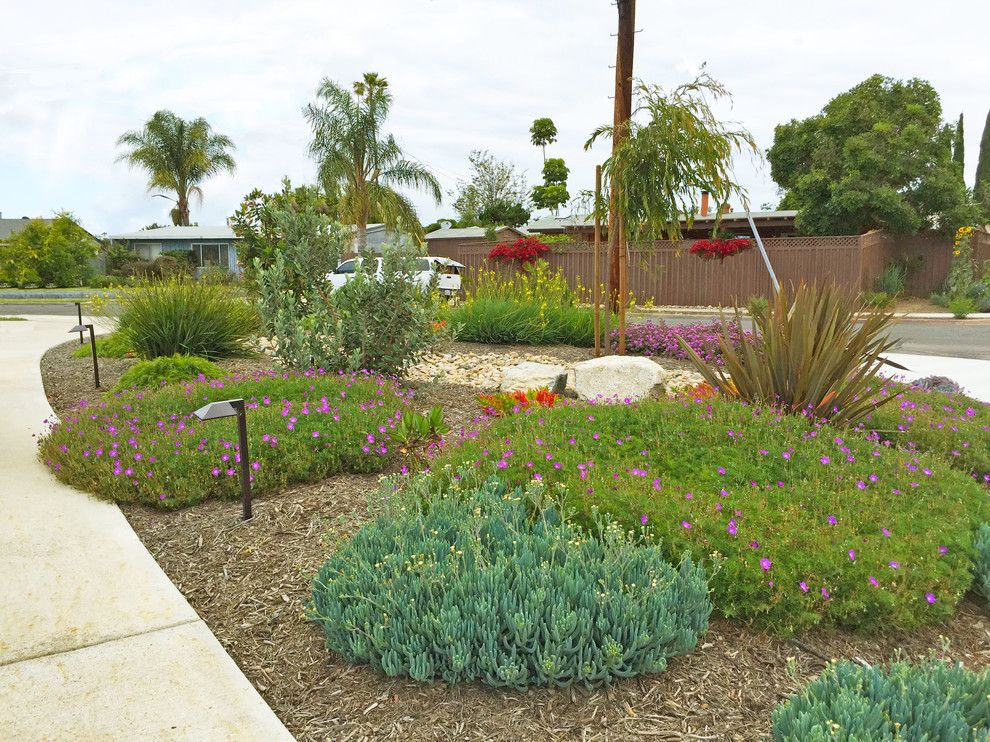 This is an example of a mid-sized transitional front yard full sun driveway for summer in San Diego with mulch, with rock feature and a wood fence.