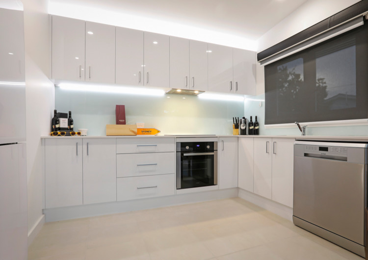 Small contemporary u-shaped open plan kitchen in Central Coast with a single-bowl sink, louvered cabinets, white cabinets, quartzite benchtops, white splashback, glass sheet splashback, stainless steel appliances, ceramic floors, no island and beige floor.