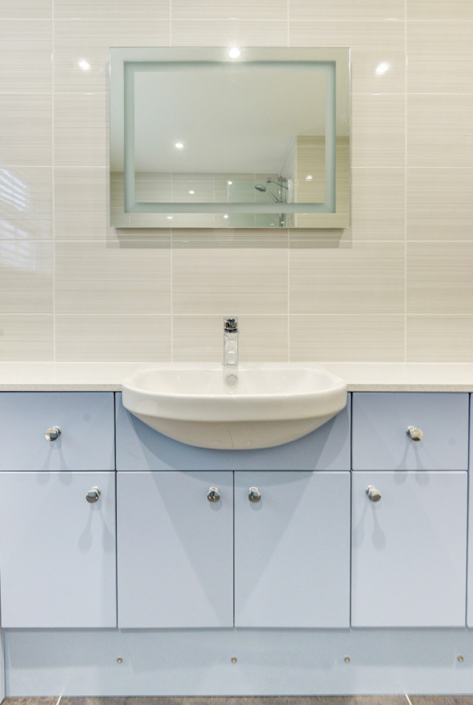 Inredning av ett modernt mellanstort vit vitt badrum för barn, med släta luckor, blå skåp, ett badkar i en alkov, en dusch/badkar-kombination, en vägghängd toalettstol, beige kakel, keramikplattor, beige väggar, ett integrerad handfat, laminatbänkskiva och grått golv