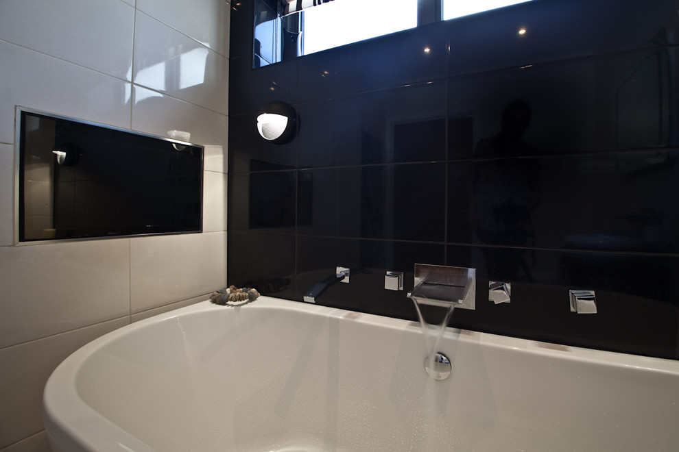 Mid-sized modern kids bathroom in Sussex with a freestanding tub, beige tile, ceramic tile and black walls.