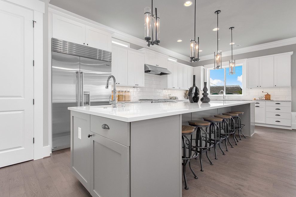 Design ideas for a large transitional l-shaped eat-in kitchen in Seattle with shaker cabinets, white cabinets, quartz benchtops, white splashback, stainless steel appliances, medium hardwood floors and with island.