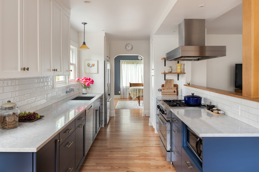 Eat-in kitchen - mid-sized traditional galley medium tone wood floor and brown floor eat-in kitchen idea in Portland with an undermount sink, shaker cabinets, blue cabinets, quartz countertops, white backsplash, subway tile backsplash, stainless steel appliances, no island and white countertops