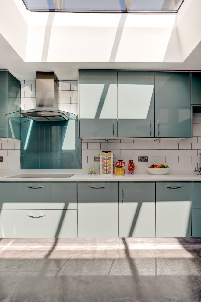 This is an example of a mid-sized eclectic l-shaped open plan kitchen in Sussex with an undermount sink, flat-panel cabinets, blue cabinets, solid surface benchtops, white splashback, ceramic splashback, stainless steel appliances, concrete floors, grey floor, white benchtop and coffered.