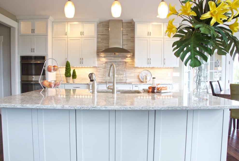 Eat-in kitchen - mid-sized transitional galley eat-in kitchen idea with white cabinets, granite countertops, beige backsplash, stone tile backsplash and stainless steel appliances