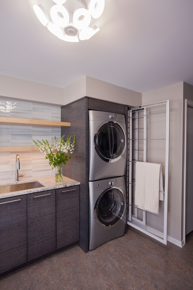 Inspiration for a mid-sized modern laundry room in Minneapolis with an undermount sink, flat-panel cabinets, grey cabinets, granite benchtops, laminate floors, a stacked washer and dryer, multi-coloured floor and grey walls.