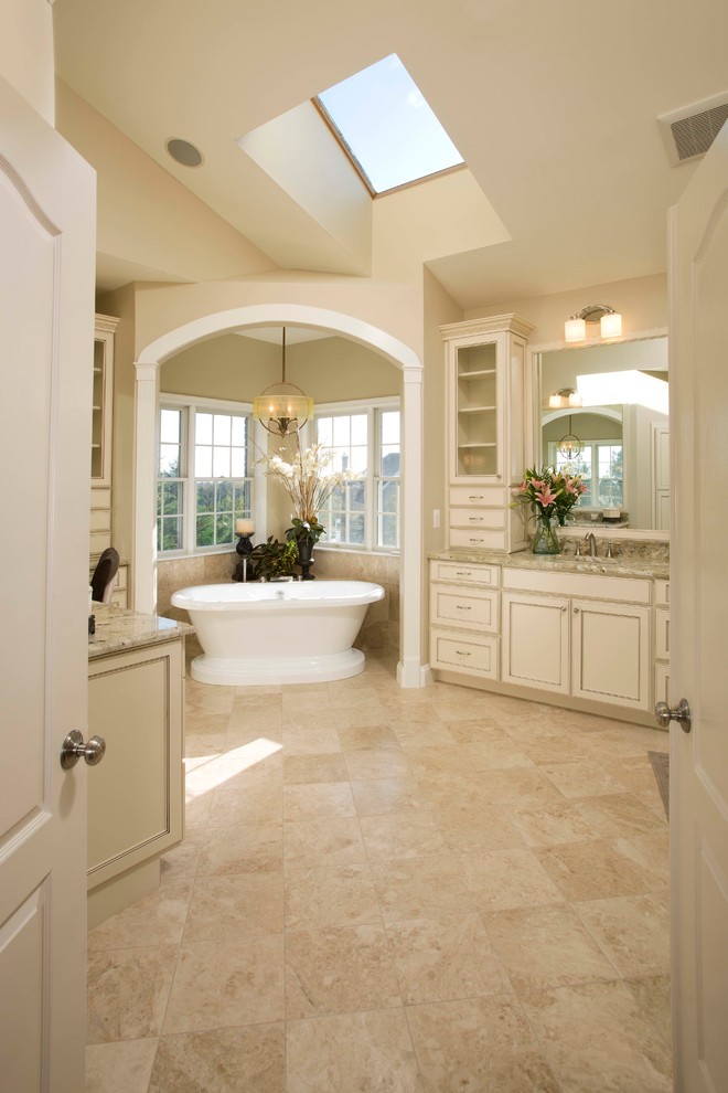Design ideas for a large traditional master bathroom in DC Metro with recessed-panel cabinets, beige cabinets, a freestanding tub, a two-piece toilet, beige tile, travertine, beige walls, travertine floors, an undermount sink, granite benchtops and beige floor.