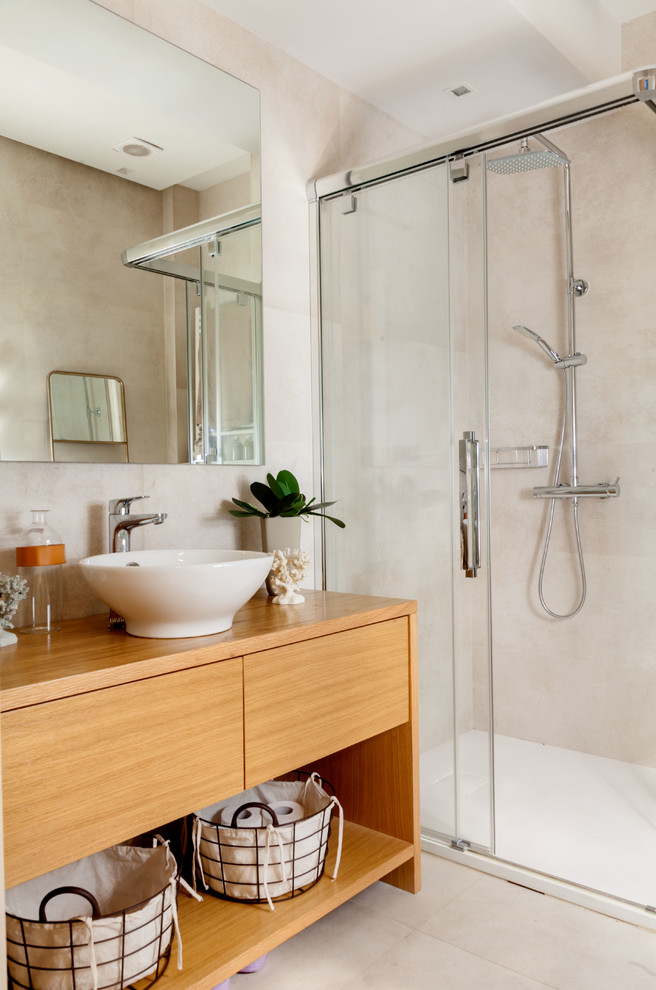 This is an example of a contemporary bathroom in Bilbao with open cabinets, medium wood cabinets, a corner shower, beige tile, a vessel sink, wood benchtops, a sliding shower screen, beige walls, beige floor and brown benchtops.