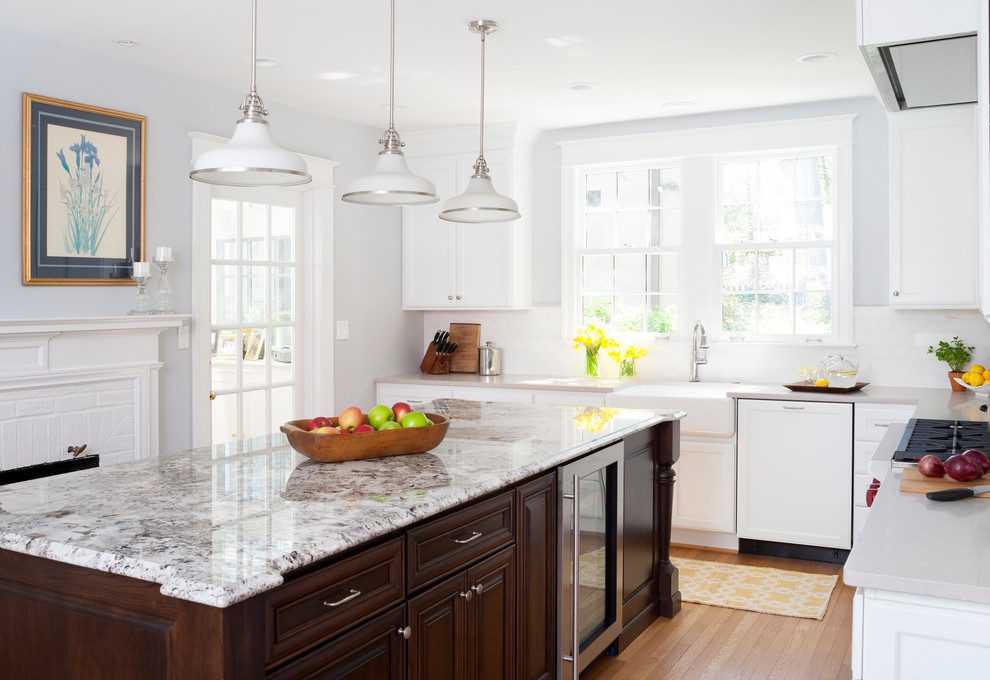 This is an example of a traditional l-shaped kitchen in DC Metro with a farmhouse sink, white cabinets, granite benchtops, light hardwood floors, with island, recessed-panel cabinets, white splashback and panelled appliances.
