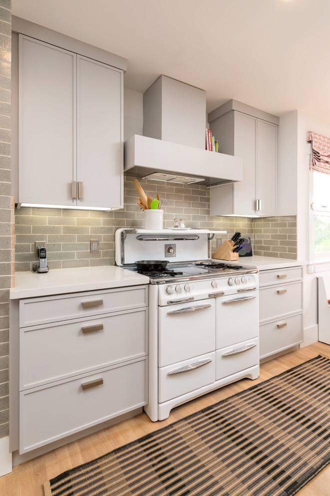 This is an example of a small eclectic l-shaped eat-in kitchen in San Francisco with a drop-in sink, recessed-panel cabinets, grey cabinets, quartz benchtops, green splashback, ceramic splashback, white appliances, medium hardwood floors and with island.