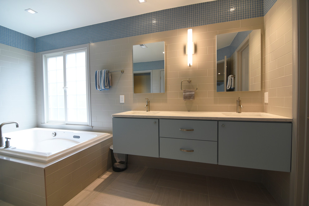 Photo of a large contemporary master bathroom in Baltimore with flat-panel cabinets, blue cabinets, a drop-in tub, a corner shower, a one-piece toilet, blue tile, glass tile, multi-coloured walls, porcelain floors, an undermount sink and engineered quartz benchtops.