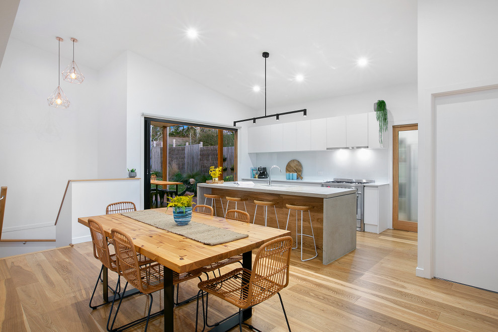 Design ideas for a mid-sized modern galley open plan kitchen in Melbourne with an undermount sink, flat-panel cabinets, white cabinets, concrete benchtops, white splashback, glass sheet splashback, stainless steel appliances, medium hardwood floors, with island, beige floor, grey benchtop and vaulted.