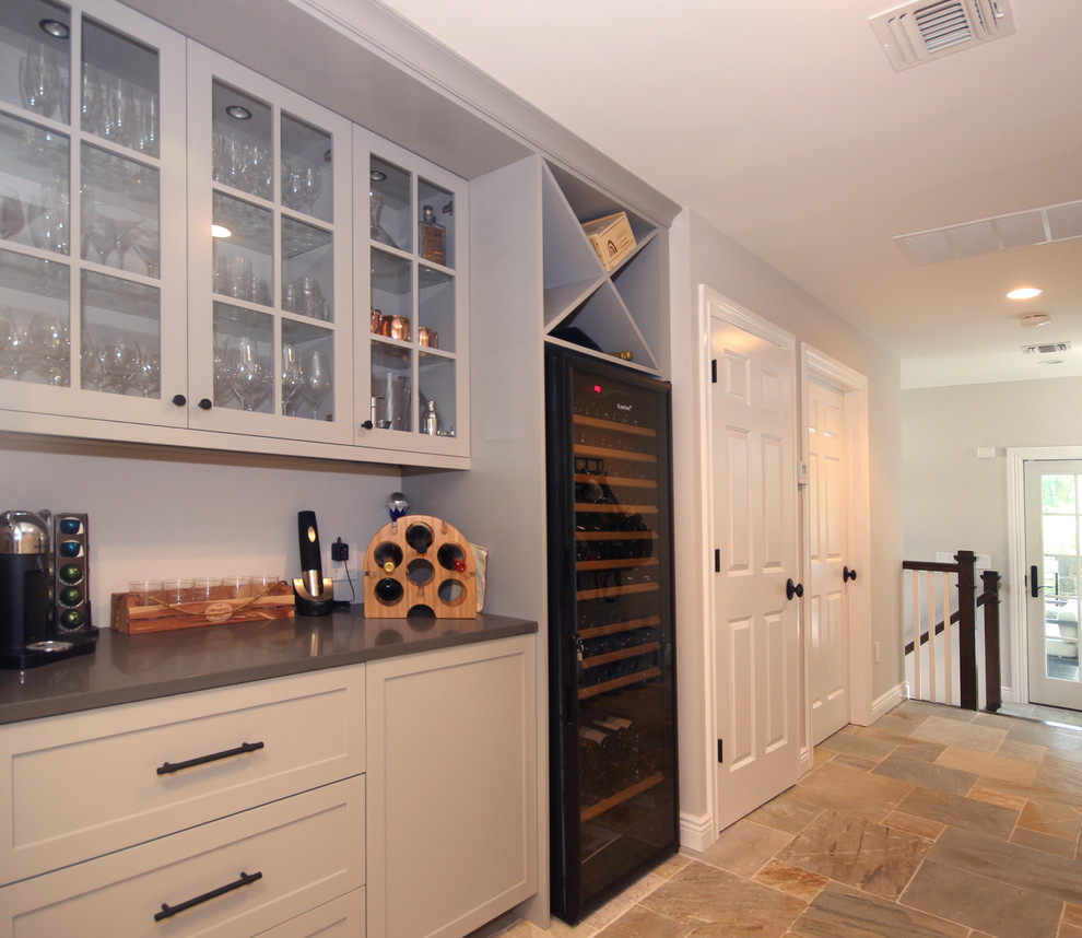 Photo of a small transitional single-wall home bar in New York with shaker cabinets, white cabinets, solid surface benchtops, slate floors and grey benchtop.