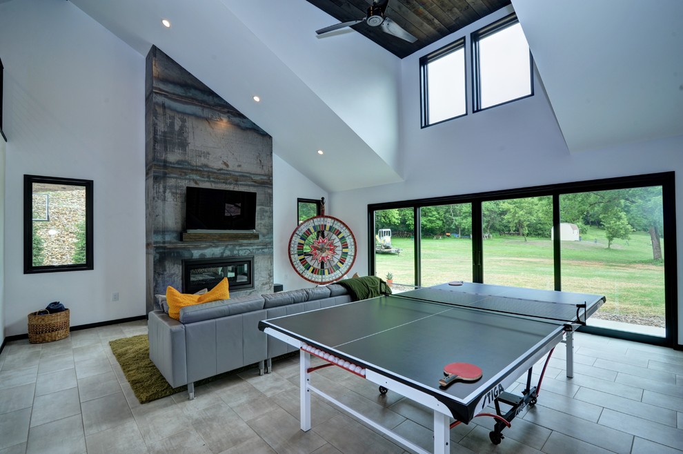 Photo of an industrial loft-style family room in Other with a game room, white walls, ceramic floors, a standard fireplace, a metal fireplace surround, a wall-mounted tv and grey floor.