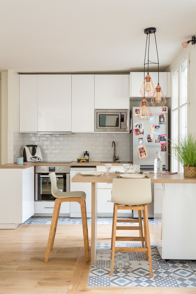 Contemporary l-shaped open plan kitchen in Paris with a drop-in sink, flat-panel cabinets, white cabinets, white splashback, subway tile splashback, stainless steel appliances, ceramic floors, a peninsula and multi-coloured floor.