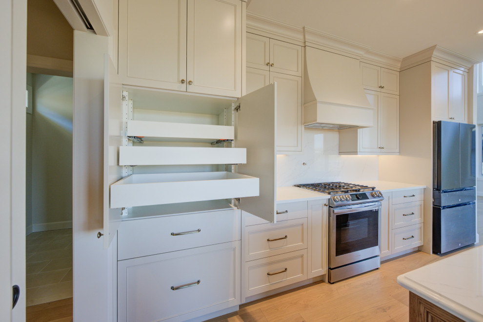 Example of a mid-sized transitional single-wall light wood floor open concept kitchen design in Toronto with an undermount sink, shaker cabinets, white cabinets, quartz countertops, white backsplash, quartz backsplash, stainless steel appliances, an island and white countertops