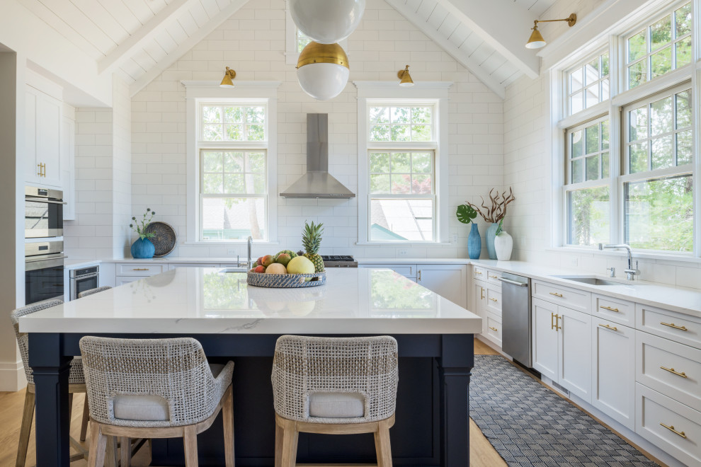 Photo of a large beach style u-shaped kitchen in Boston with an undermount sink, shaker cabinets, white cabinets, white splashback, porcelain splashback, with island, beige floor, white benchtop and wood.