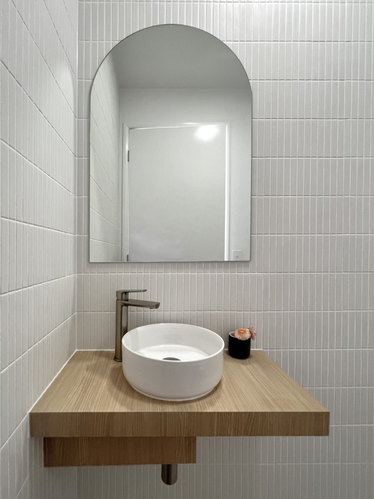 На фото: туалет в современном стиле с светлыми деревянными фасадами, унитазом-моноблоком, серой плиткой, удлиненной плиткой, белыми стенами, полом из керамической плитки, столешницей из ламината, серым полом и подвесной тумбой с