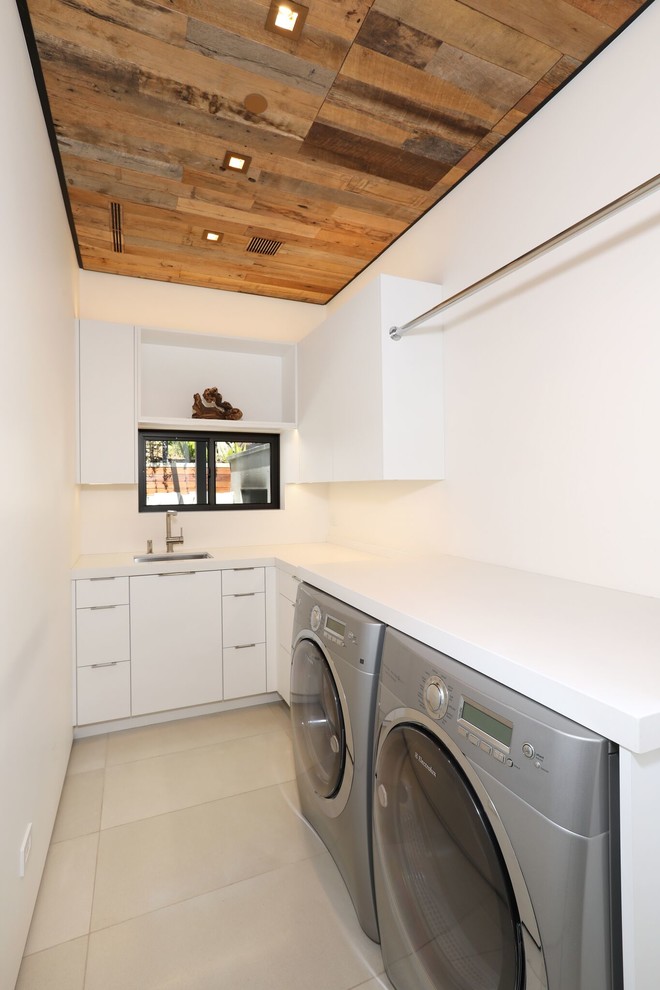 Inspiration for a mid-sized contemporary l-shaped dedicated laundry room in Orange County with an undermount sink, flat-panel cabinets, white cabinets, quartz benchtops, white walls, concrete floors, a side-by-side washer and dryer, beige floor and white benchtop.