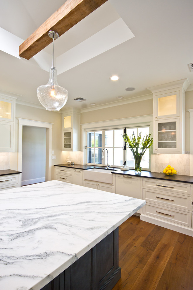 Large transitional u-shaped medium tone wood floor eat-in kitchen photo in Phoenix with a farmhouse sink, recessed-panel cabinets, white cabinets, marble countertops, white backsplash, stone tile backsplash, stainless steel appliances and an island