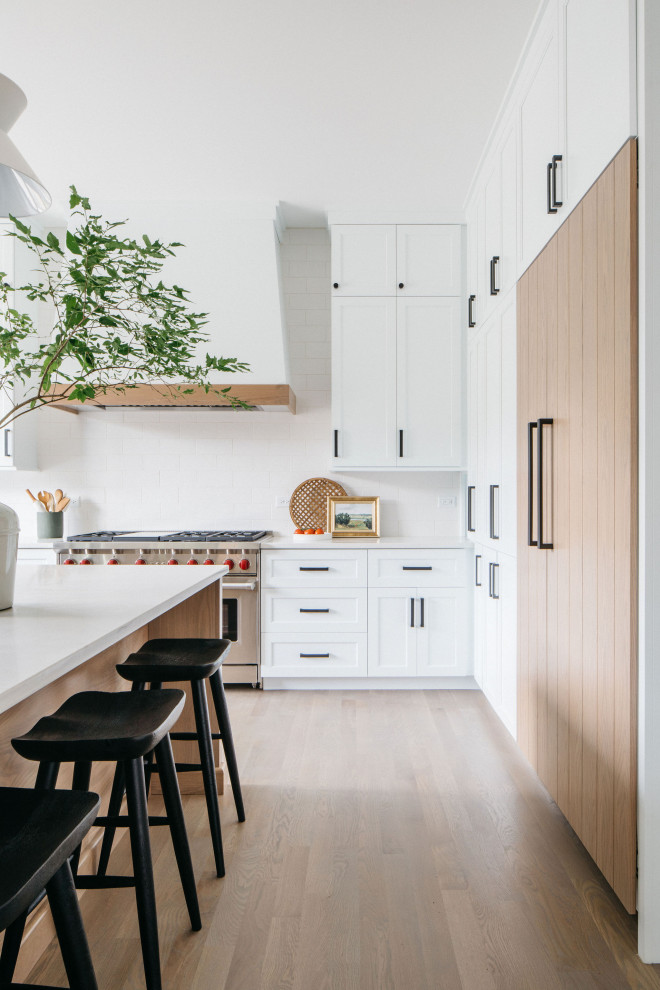 This is an example of a large rural u-shaped kitchen/diner in Chicago with shaker cabinets, white cabinets, white splashback, stainless steel appliances, an island, white worktops and beige floors.