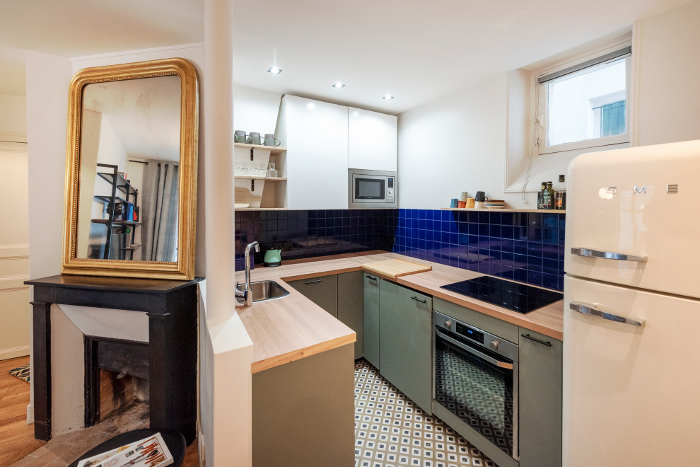 Foto på ett litet funkis kök, med luckor med profilerade fronter, gröna skåp, träbänkskiva, blått stänkskydd, stänkskydd i keramik och cementgolv