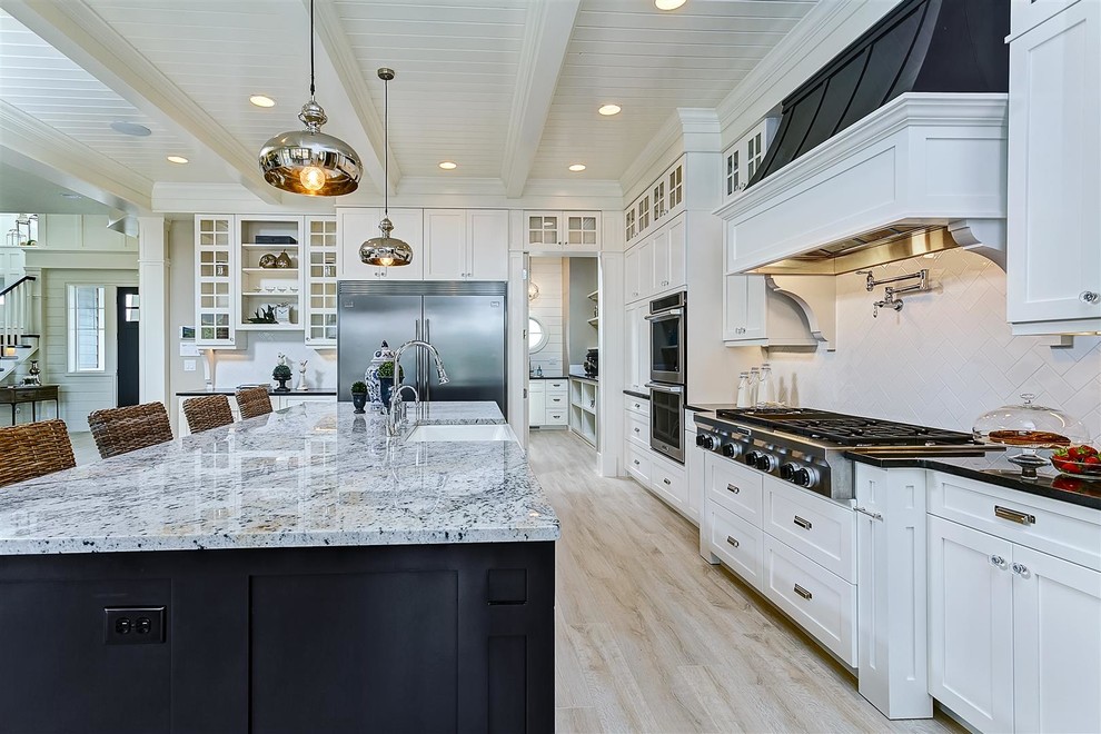 Photo of a large traditional l-shaped open plan kitchen in Boise with a farmhouse sink, shaker cabinets, white cabinets, granite benchtops, white splashback, ceramic splashback, stainless steel appliances, light hardwood floors and with island.