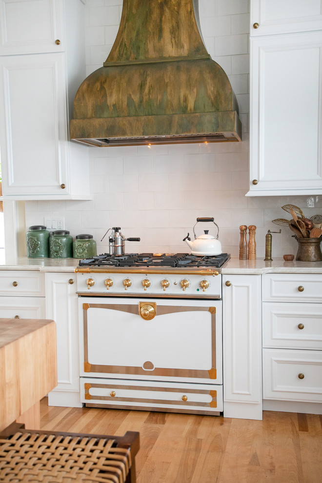 This is an example of a large country u-shaped eat-in kitchen in Milwaukee with a farmhouse sink, recessed-panel cabinets, white cabinets, white splashback, white appliances, light hardwood floors, with island, beige floor and white benchtop.
