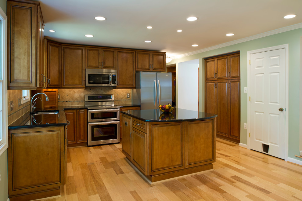 Inspiration for a mid-sized traditional l-shaped open plan kitchen in DC Metro with an undermount sink, raised-panel cabinets, medium wood cabinets, granite benchtops, beige splashback, stone tile splashback, stainless steel appliances, light hardwood floors and with island.