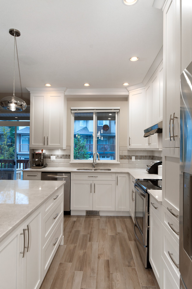 Eat-in kitchen - mid-sized transitional l-shaped light wood floor eat-in kitchen idea in Vancouver with an undermount sink, shaker cabinets, white cabinets, quartz countertops, white backsplash, ceramic backsplash, stainless steel appliances and an island
