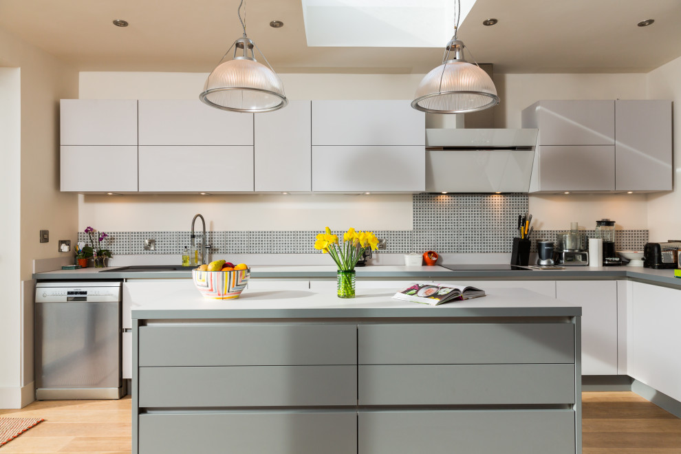 Medium sized contemporary l-shaped kitchen/diner in Hampshire with a single-bowl sink, flat-panel cabinets, grey cabinets, laminate countertops, grey splashback, ceramic splashback, stainless steel appliances, light hardwood flooring and an island.