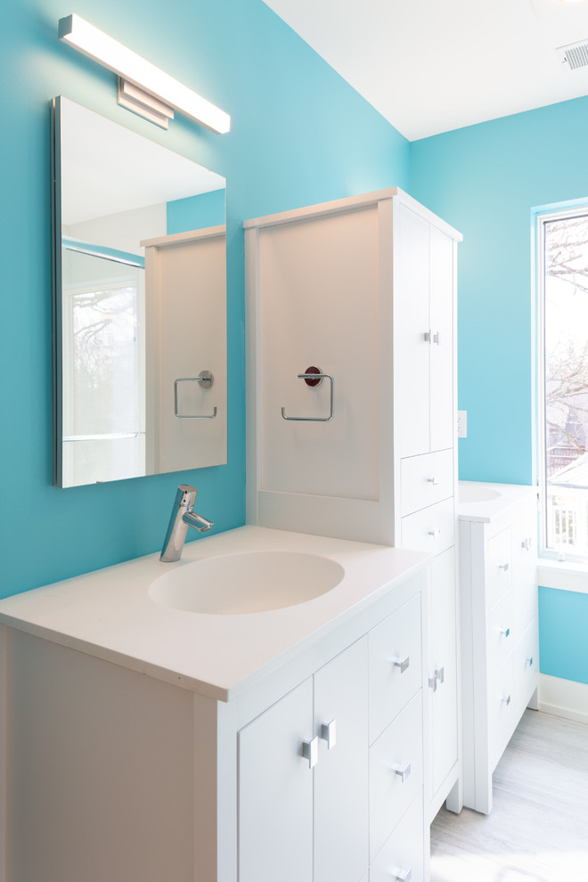 Design ideas for a mid-sized modern kids bathroom in Detroit with flat-panel cabinets, white cabinets, blue walls, laminate floors, an integrated sink, engineered quartz benchtops, white floor and white benchtops.