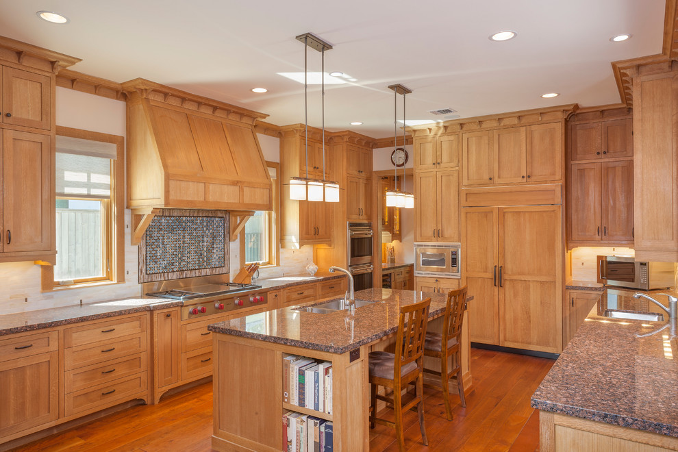 This is an example of a large arts and crafts u-shaped eat-in kitchen in Houston with an undermount sink, shaker cabinets, medium wood cabinets, granite benchtops, beige splashback, glass tile splashback, stainless steel appliances, medium hardwood floors and with island.
