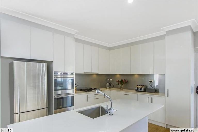 This is an example of a mid-sized modern l-shaped eat-in kitchen in Sydney with an undermount sink, flat-panel cabinets, white cabinets, quartzite benchtops, metallic splashback, glass sheet splashback, stainless steel appliances, bamboo floors and with island.
