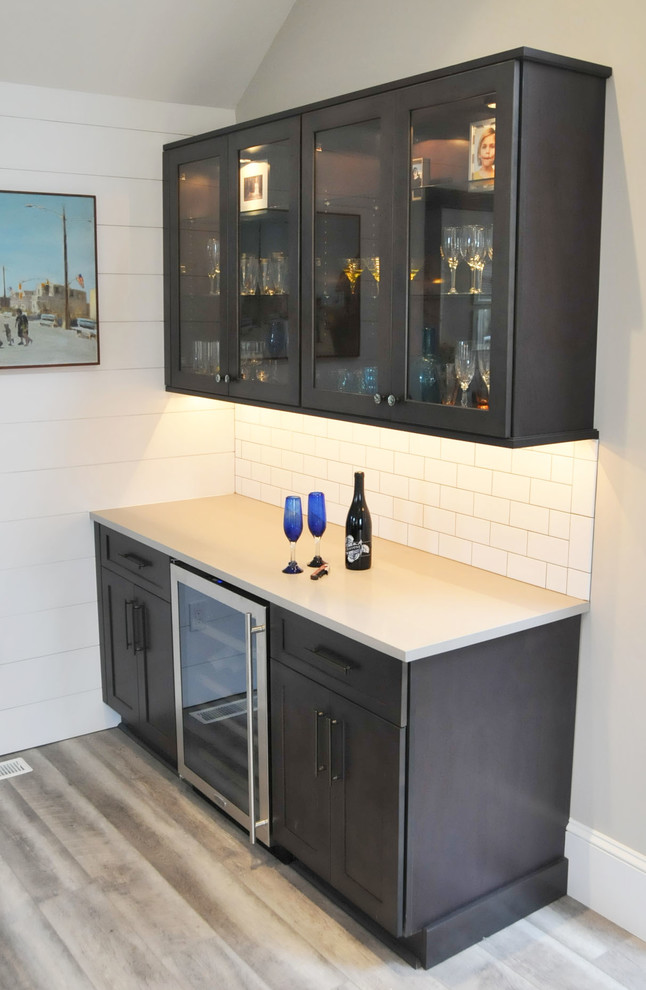 Design ideas for a mid-sized contemporary single-wall wet bar in Philadelphia with no sink, glass-front cabinets, dark wood cabinets, solid surface benchtops, white splashback, subway tile splashback, light hardwood floors, grey floor and beige benchtop.