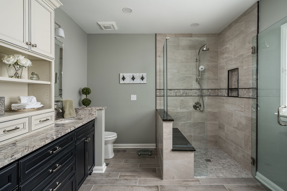 Photo of a large traditional master bathroom in Columbus with recessed-panel cabinets, black cabinets, a curbless shower, a one-piece toilet, gray tile, grey walls, an undermount sink, granite benchtops, multi-coloured floor, a hinged shower door, white benchtops, a shower seat, a double vanity and a freestanding vanity.