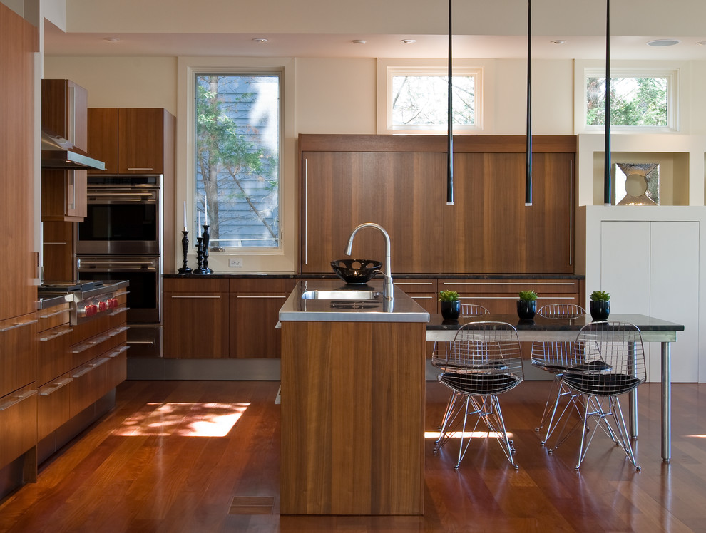 Photo of a mid-sized contemporary u-shaped eat-in kitchen in Baltimore with an integrated sink, flat-panel cabinets, dark wood cabinets, stainless steel benchtops, stainless steel appliances, medium hardwood floors and with island.