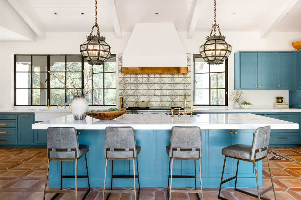 This is an example of a mediterranean u-shaped eat-in kitchen in San Francisco with a farmhouse sink, shaker cabinets, blue cabinets, marble benchtops, multi-coloured splashback, stainless steel appliances, terra-cotta floors, with island, brown floor, multi-coloured benchtop and exposed beam.