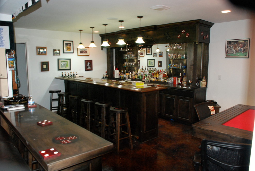 This is an example of a large traditional galley seated home bar in Seattle with raised-panel cabinets, dark wood cabinets, wood benchtops, mirror splashback and concrete floors.