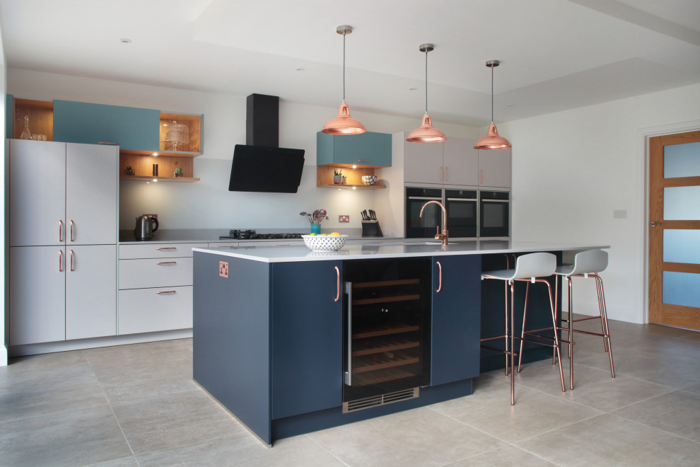 Large contemporary galley kitchen in Buckinghamshire with an undermount sink, flat-panel cabinets, grey cabinets, black appliances, with island, grey floor and white benchtop.
