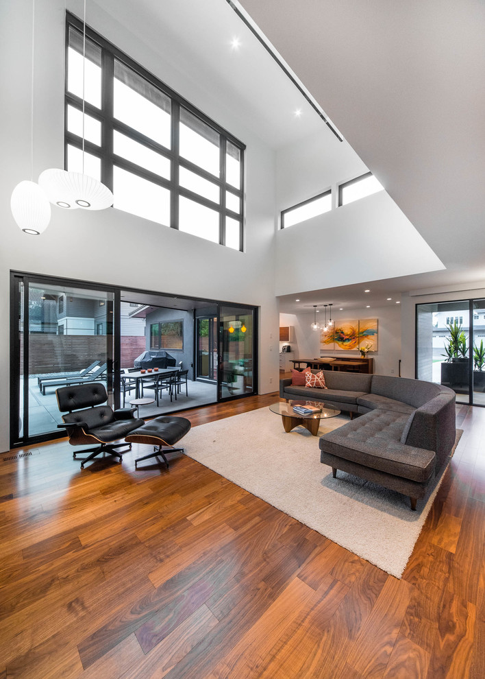 This is an example of a large midcentury loft-style living room in Vancouver with white walls, medium hardwood floors, a standard fireplace, a tile fireplace surround, a wall-mounted tv and brown floor.