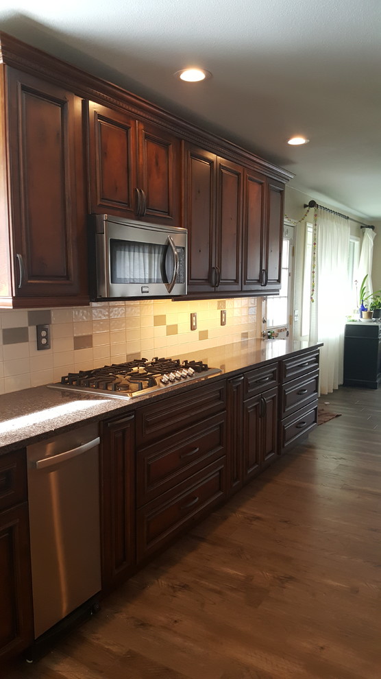Kitchen - large transitional galley laminate floor kitchen idea with an undermount sink, raised-panel cabinets, distressed cabinets, quartz countertops, white backsplash, ceramic backsplash, stainless steel appliances and an island
