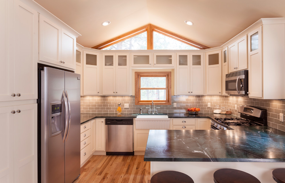 This is an example of a traditional u-shaped kitchen in Denver with glass-front cabinets, stainless steel appliances, subway tile splashback, a farmhouse sink and soapstone benchtops.
