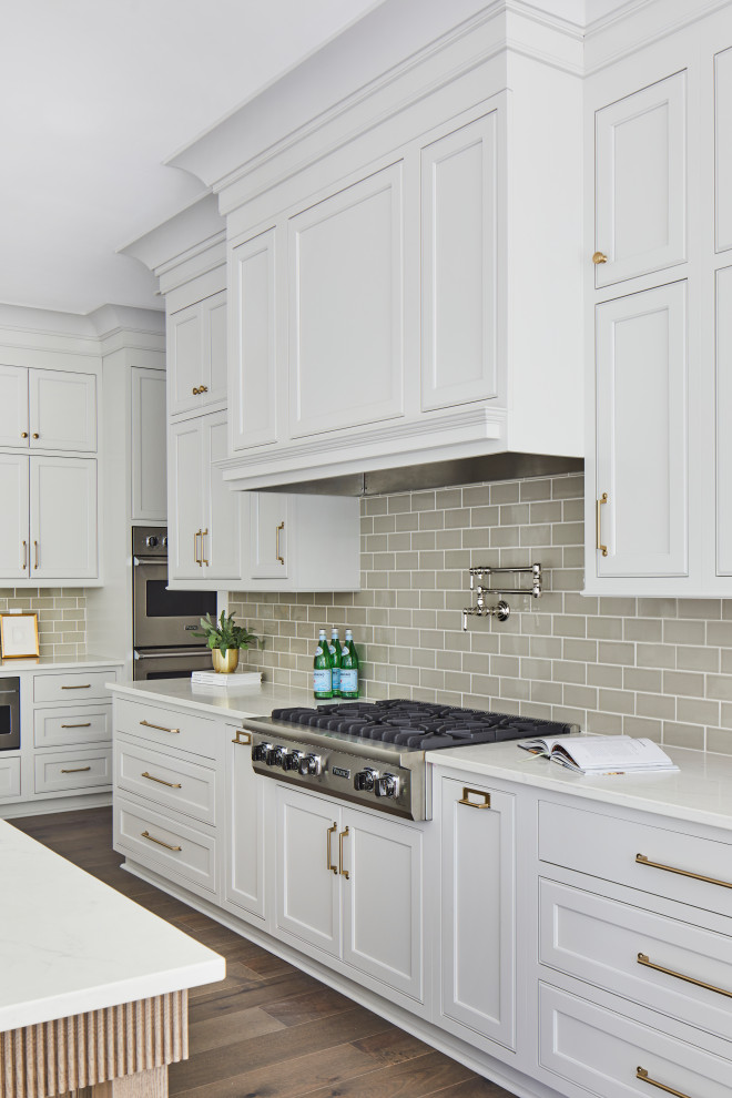 Large transitional l-shaped kitchen in Birmingham with a farmhouse sink, recessed-panel cabinets, white cabinets, grey splashback, ceramic splashback, stainless steel appliances, dark hardwood floors, with island and white benchtop.