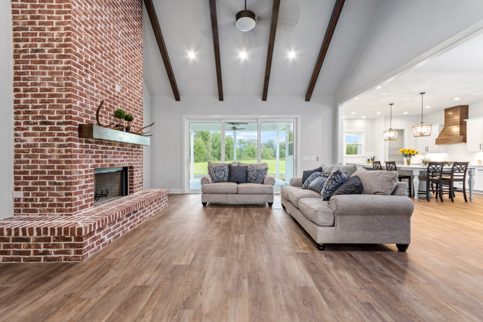 Design ideas for a medium sized country open plan games room in Other with grey walls, vinyl flooring, a standard fireplace, a brick fireplace surround, a wall mounted tv, brown floors and a vaulted ceiling.