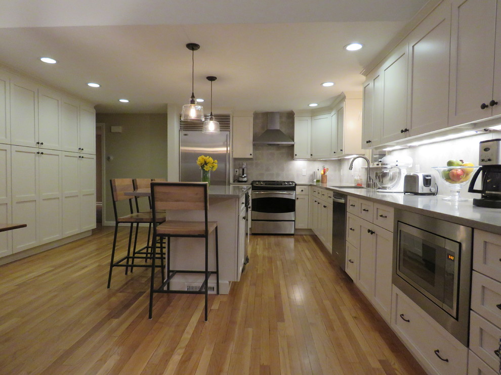 Inspiration for a large transitional l-shaped medium tone wood floor open concept kitchen remodel in Boston with an undermount sink, shaker cabinets, white cabinets, quartz countertops, gray backsplash, stainless steel appliances and an island