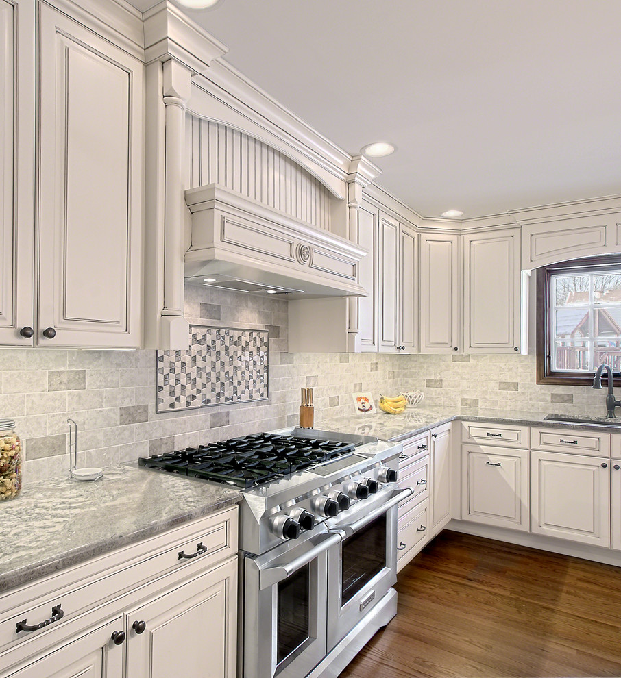 Photo of a large transitional u-shaped eat-in kitchen in Chicago with a drop-in sink, raised-panel cabinets, white cabinets, granite benchtops, grey splashback, ceramic splashback, stainless steel appliances, dark hardwood floors, with island and brown floor.