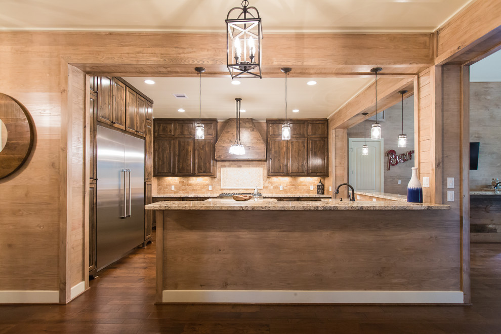 Large country u-shaped open plan kitchen in Houston with a farmhouse sink, raised-panel cabinets, dark wood cabinets, granite benchtops, beige splashback, ceramic splashback, stainless steel appliances, medium hardwood floors, with island and brown floor.