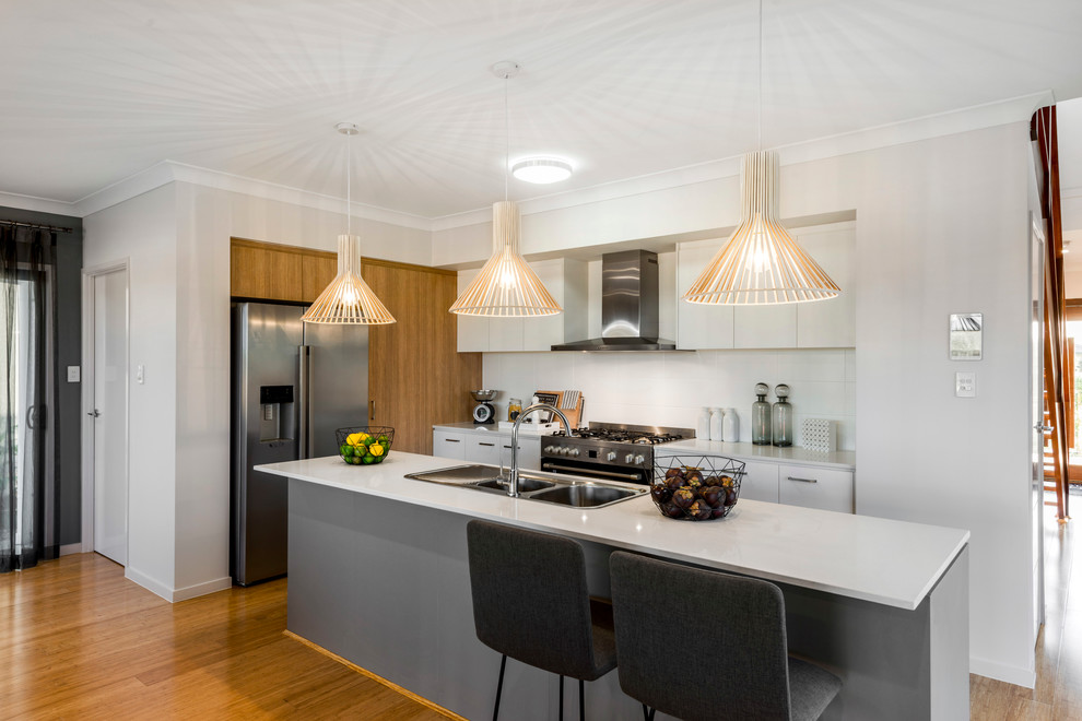 Mid-sized contemporary galley eat-in kitchen in Brisbane with a double-bowl sink, flat-panel cabinets, light wood cabinets, quartz benchtops, grey splashback, ceramic splashback, stainless steel appliances, bamboo floors and with island.