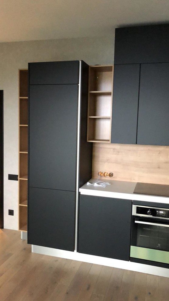 This is an example of a mid-sized contemporary single-wall eat-in kitchen in Other with an undermount sink, flat-panel cabinets, black cabinets, laminate benchtops, beige splashback, timber splashback, black appliances, medium hardwood floors, multiple islands, beige floor and white benchtop.