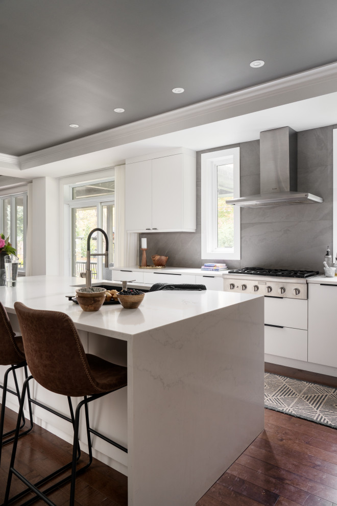 Photo of a large transitional u-shaped eat-in kitchen in Montreal with an undermount sink, flat-panel cabinets, white cabinets, quartz benchtops, grey splashback, slate splashback, stainless steel appliances, dark hardwood floors, with island, brown floor, white benchtop and coffered.